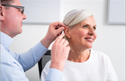 Hörakustiker passt einer Frau ein Hörgerät an